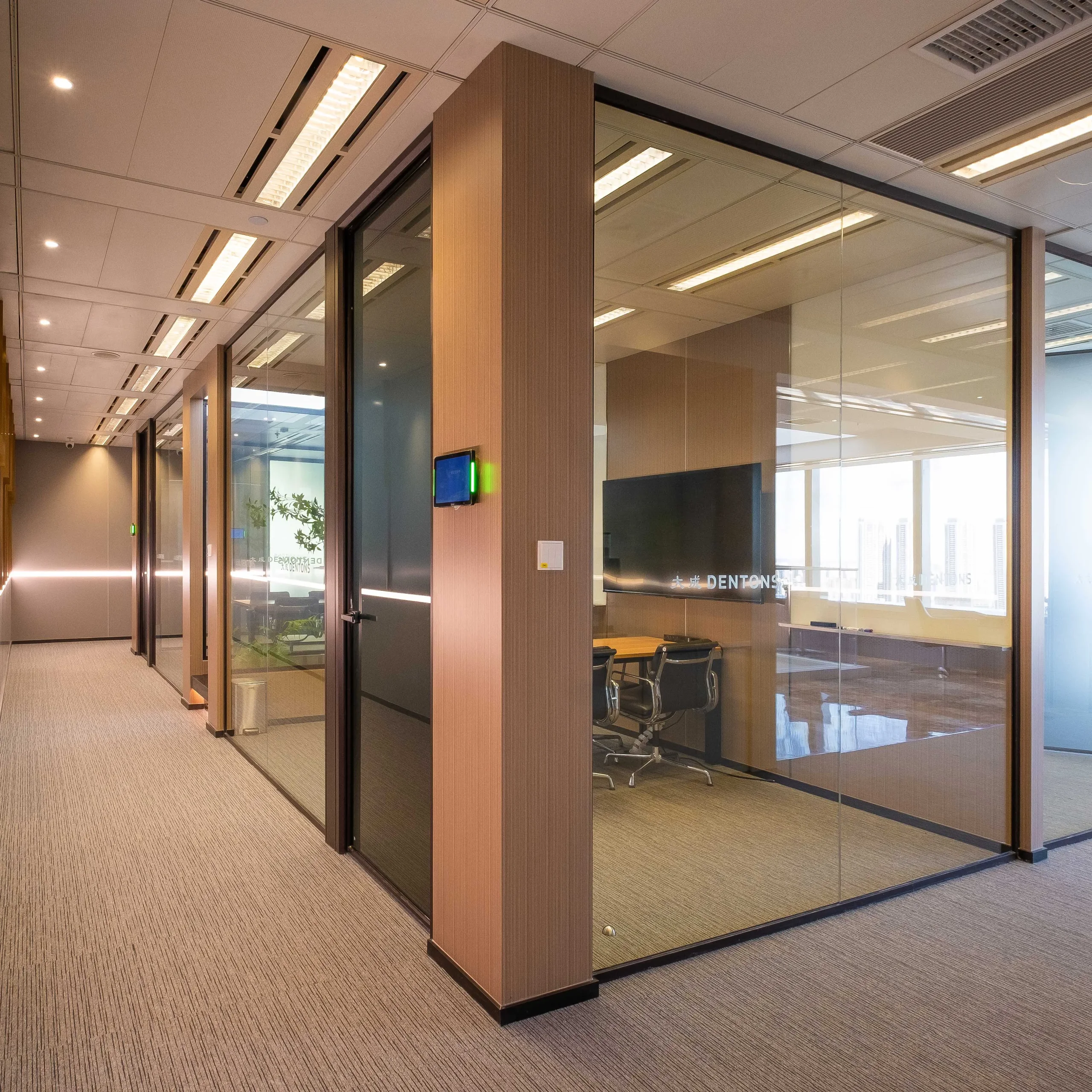 Office partition systems in a large-pane configuration — floor-to-ceiling glass meeting room fronts with slim dark frames and wood-clad columns in a law firm corridor