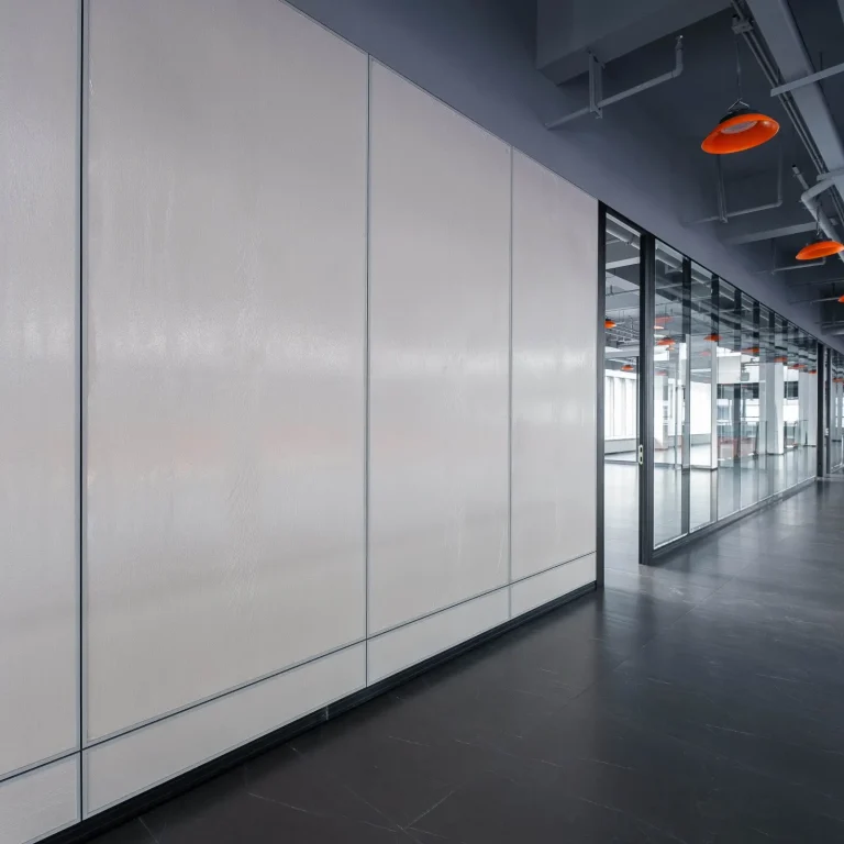 Solid panel partition wall installation along industrial-style office corridor with adjacent glass partition system and orange pendant lights